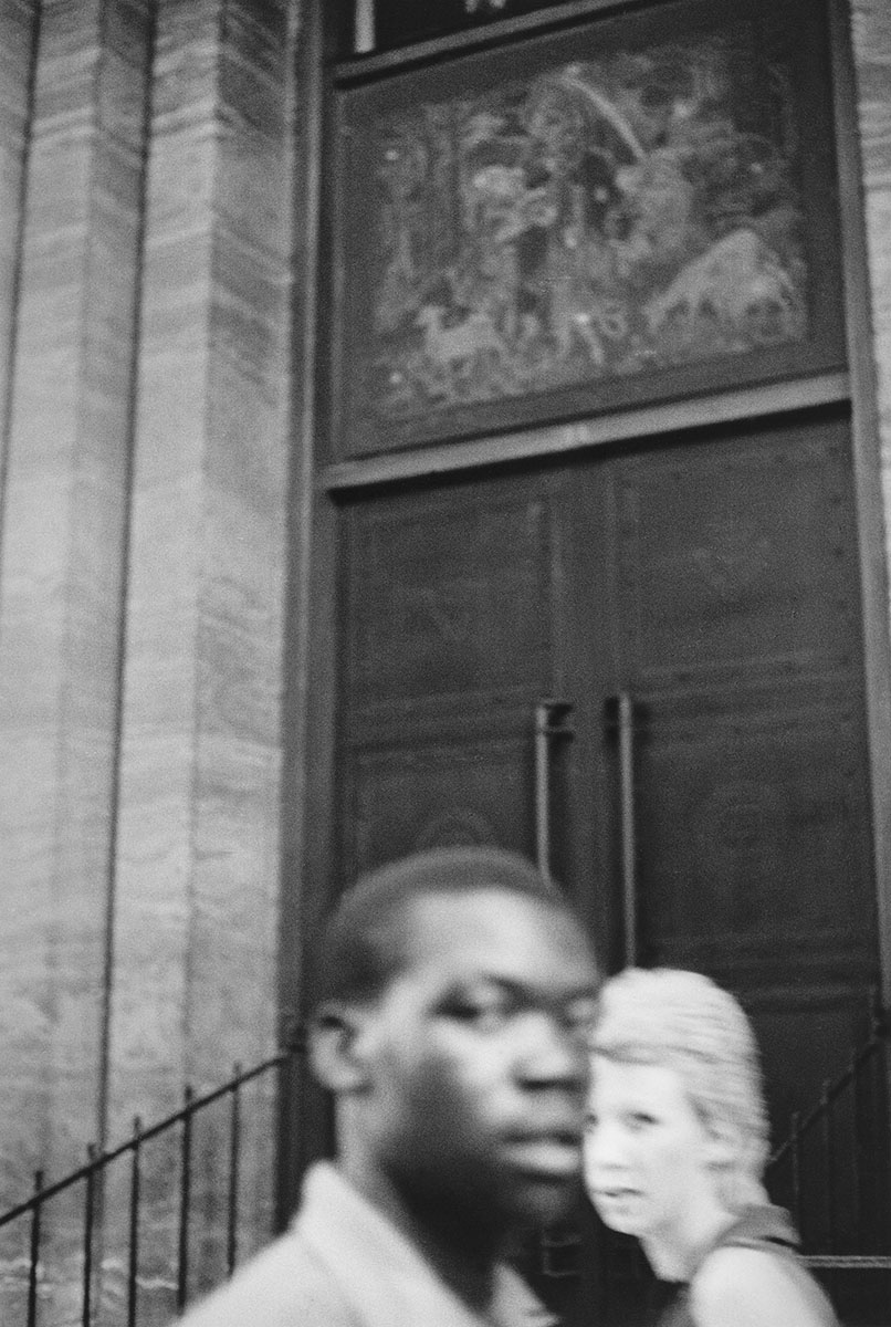 black and white image of man and woman crossing paths in front of door