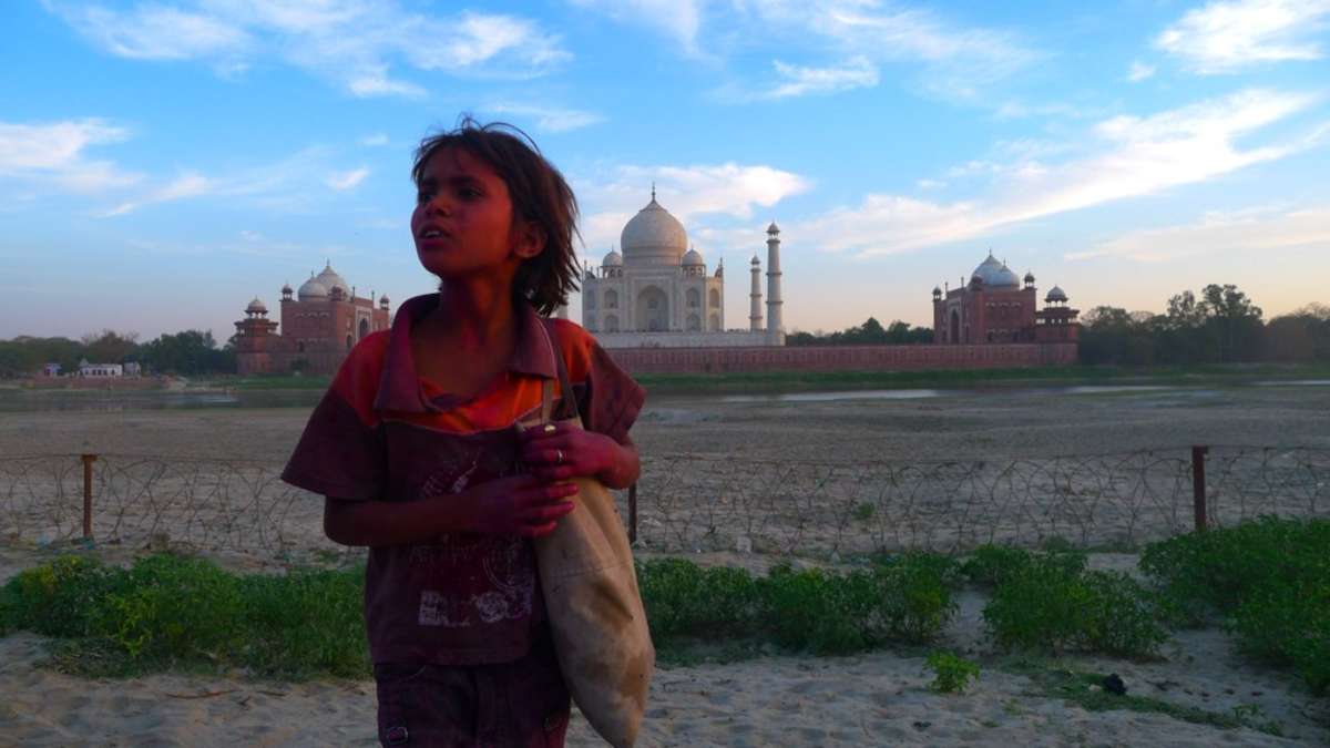 Child covered in pink paint with Taj Mahal behind in the distance