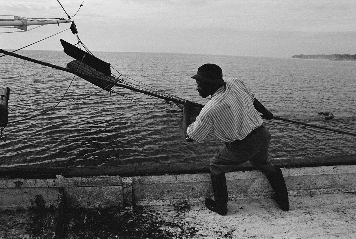 black and white image of man pulling in line on a boat